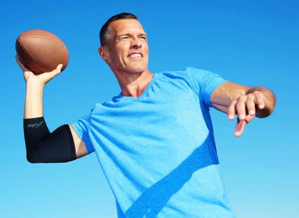 A man with a Dr. Arthritis copper-infused elbow compression sleeve throwing a football in the air.