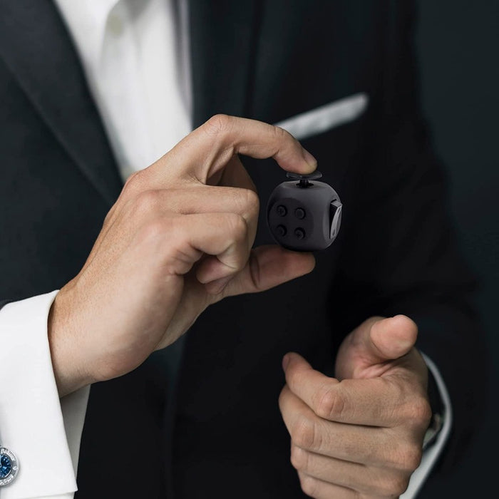 A man in a suit is holding a small black Dr. Arthritis Button Fidget Cube for Adults and All Ages.