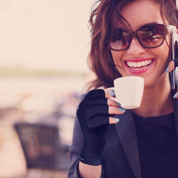 A woman holding a cup of coffee while talking on her cell phone in Dr. Arthritis Copper Compression Gloves (Open-Finger).