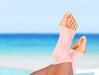 A woman's feet on the beach with a pair of Dr. Arthritis Copper Infused Foot Sleeves for compression and relief from foot conditions.