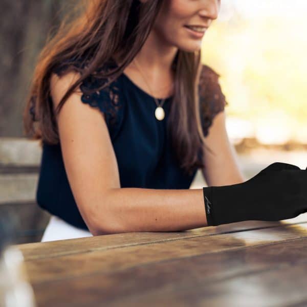 A woman sitting at a table with a cell phone wearing Dr. Arthritis Copper Compression Gloves (Full-Fingered).
