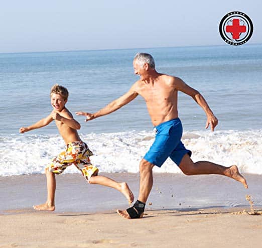 An older man and a young boy are happily running on the beach wearing Dr. Arthritis Copper Lined Ankle Support Brace.