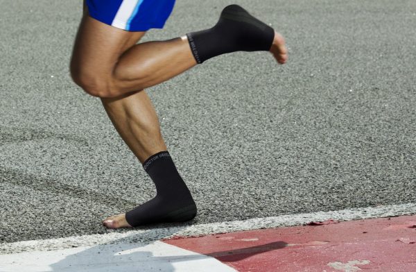 A man running on a track with a Dr. Arthritis Copper Infused Foot Sleeve (Pair) to assist with his foot condition.