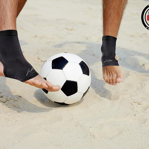 Two men playing soccer barefoot on the sand.