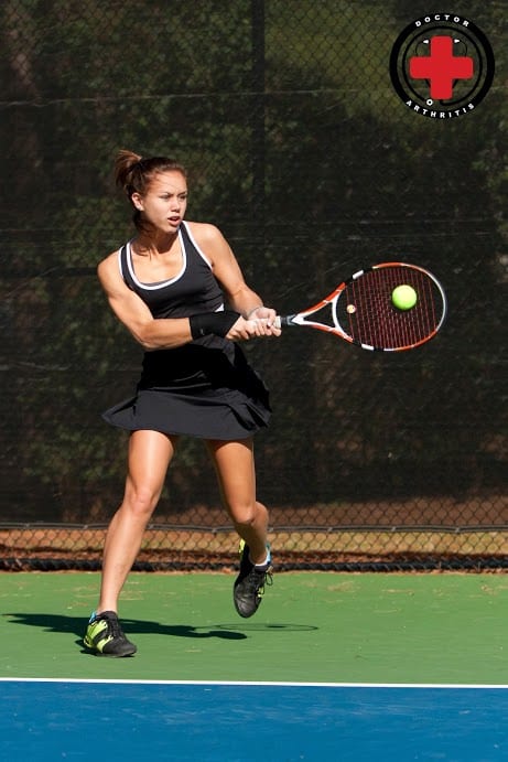 A female tennis player gracefully swings her racket at a ball with the Dr. Arthritis Copper Infused Wrist Sleeve [Single] for wrist support.