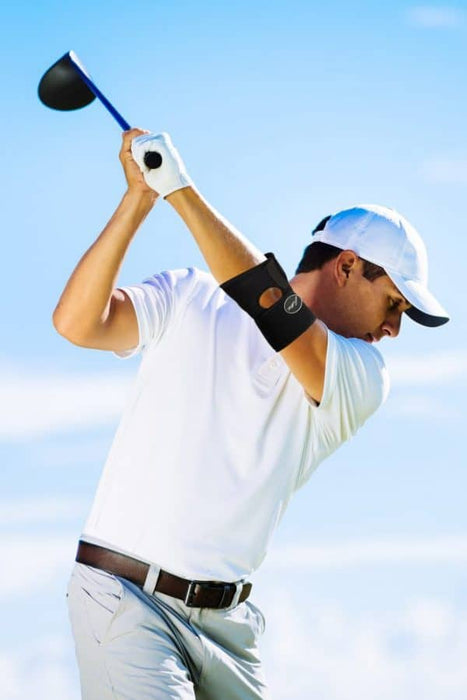 A man swinging a golf club on a sunny day with Dr. Arthritis Copper Lined Elbow Support Brace.