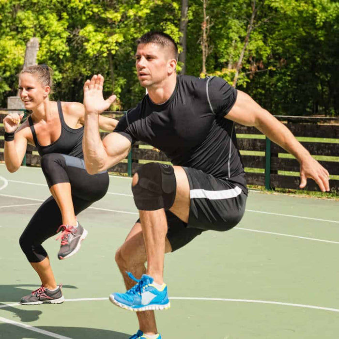 A man and woman doing squats on a basketball court while wearing a Dr. Arthritis Copper Lined Knee Support Band.
