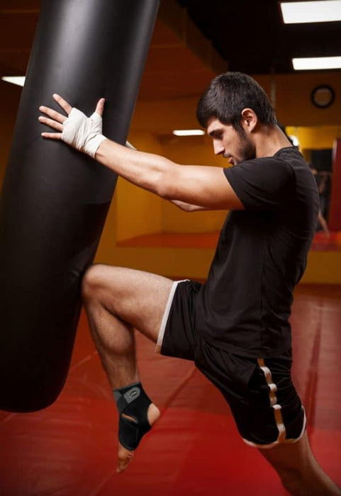 A man kicks a punching bag in the gym, showcasing his strength and agility with the Dr. Arthritis Copper Lined Ankle Support Brace.
