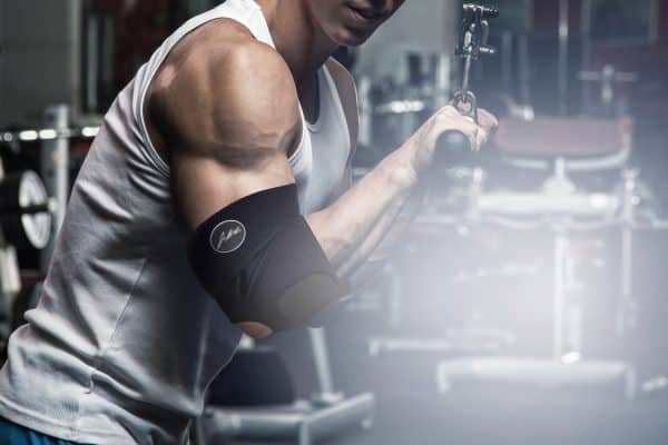 In the gym, a man is holding a barbell with the Dr. Arthritis Copper Lined Elbow Support Brace.