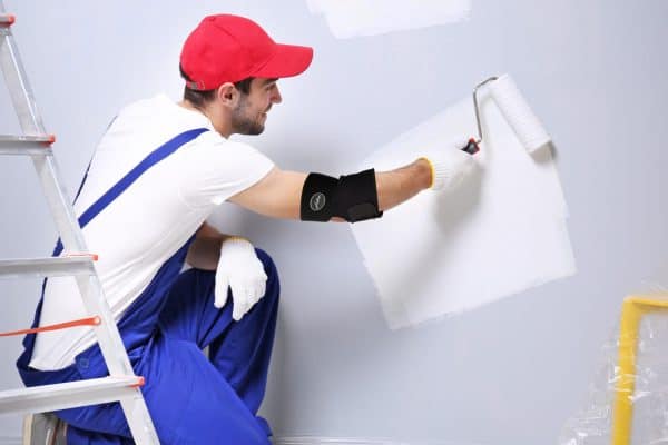 A man painting a wall with a Dr. Arthritis Copper Lined Elbow Support Brace for elbow support.