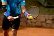 A man holding a tennis racket and a ball, with his Dr. Arthritis Copper Lined Elbow Support Brace supported.