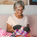 A woman sitting on a couch wearing Dr. Arthritis Compression Crochet Fingerless Gloves for arthritis relief.
