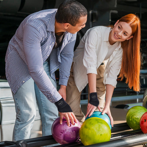 Two people playing bowling at a bowling alley with Dr. Arthritis Copper Lined Bowling Wrist Brace [Single] support.
