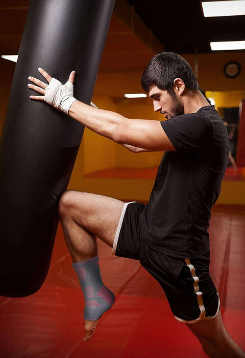 A man kicking a punching bag in a gym while wearing a Dr. Arthritis ankle compression sleeve.