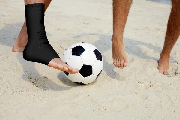 Two people kicking a soccer ball on the beach wearing Dr. Arthritis Ankle Compression Sleeves.