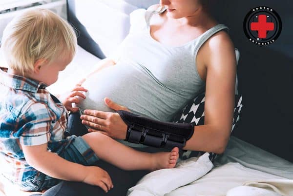 A pregnant woman experiencing wrist pain wears a Dr. Arthritis Carpal Tunnel Bundle wrist brace and sits on a couch, talking on the phone while a young boy interacts with her.