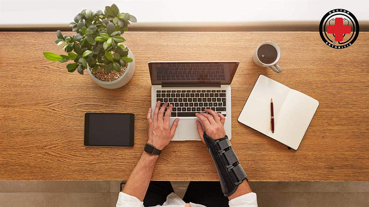 Top view of a person working on a laptop at a wooden desk with a smartphone, coffee cup, notepad, and a potted plant, potentially risking wrist pain with the Dr. Arthritis Carpal Tunnel Bundle.