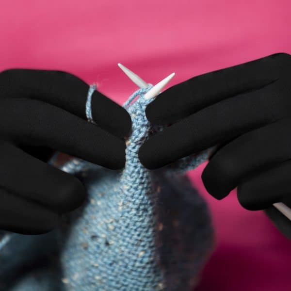 A person wearing Dr. Arthritis Copper Compression Gloves (Full-Fingered) is knitting a sweater.