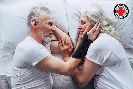 An elderly couple laying in bed with a Dr. Arthritis Carpal Tunnel Wrist Brace [Single] on their arm.