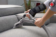 A person with a Dr. Arthritis Carpal Tunnel Wrist Brace cleaning a couch with a vacuum.