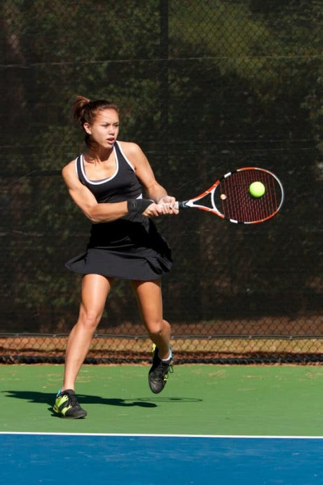 A female tennis player wearing a Dr. Arthritis Copper Lined Wrist Support [Single], swinging her racket at a ball.