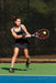 A female tennis player wearing a Dr. Arthritis Copper Lined Wrist Support [Single], swinging her racket at a ball.