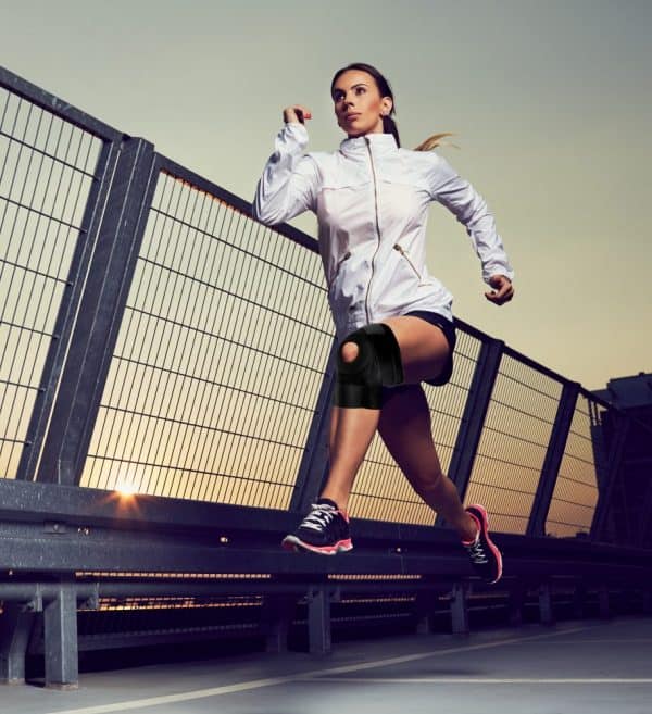A woman running on a bridge at sunset wearing a Dr. Arthritis Copper Lined Knee Support Band.